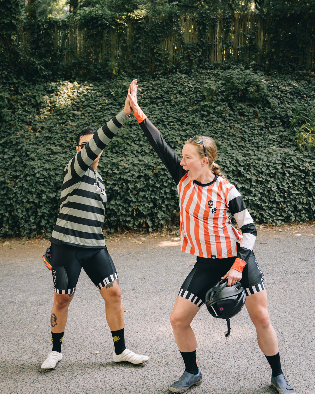 two friends high fiving in cycling gear on a forest trail.