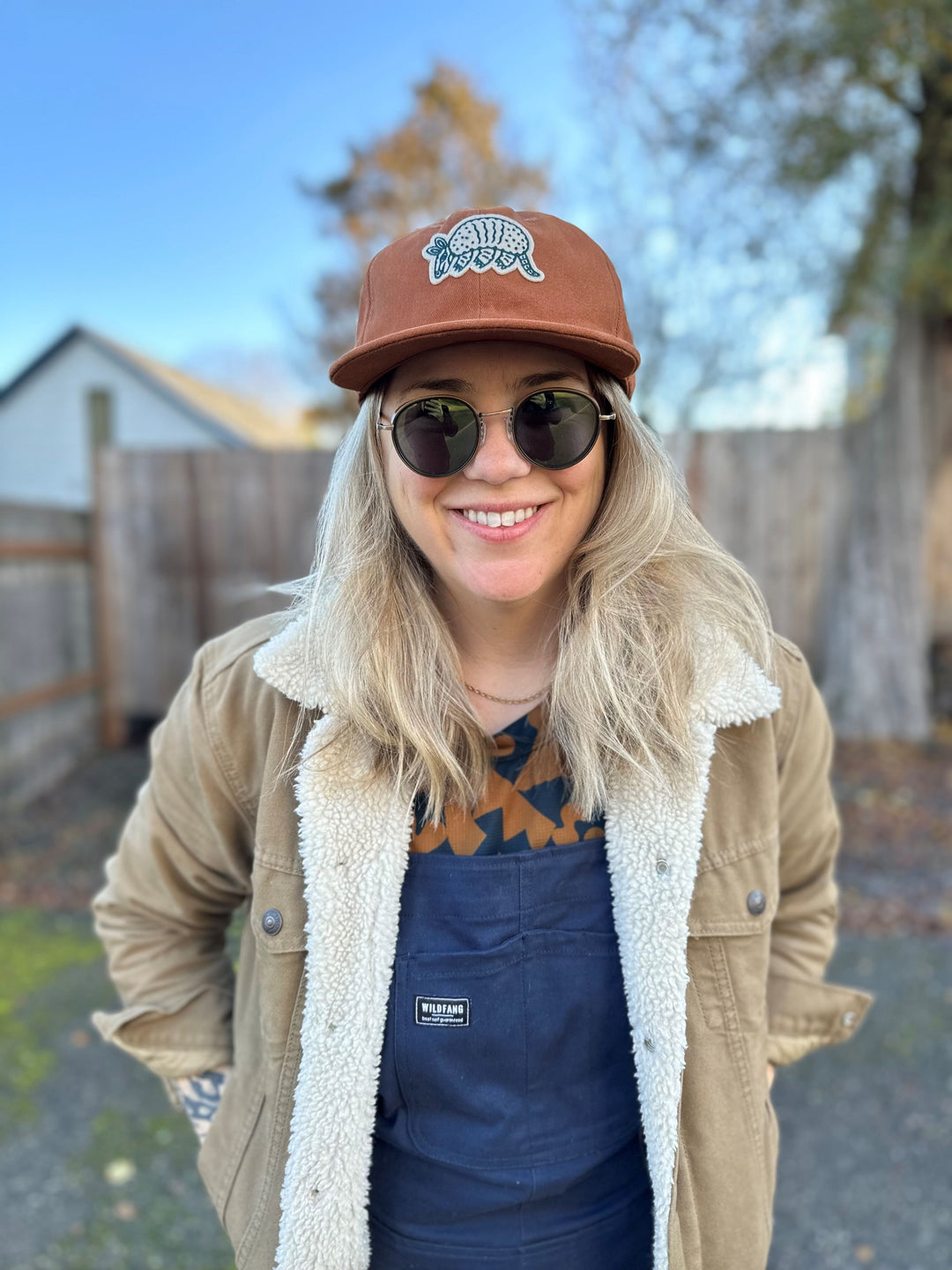 The Athletic Armadillo Logo Hat in rust features an unstructured 6-panel design with an adjustable fabric strap and brass metal clasp. Embroidered with a stylized armadillo logo, this hat combines comfort and style for everyday wear