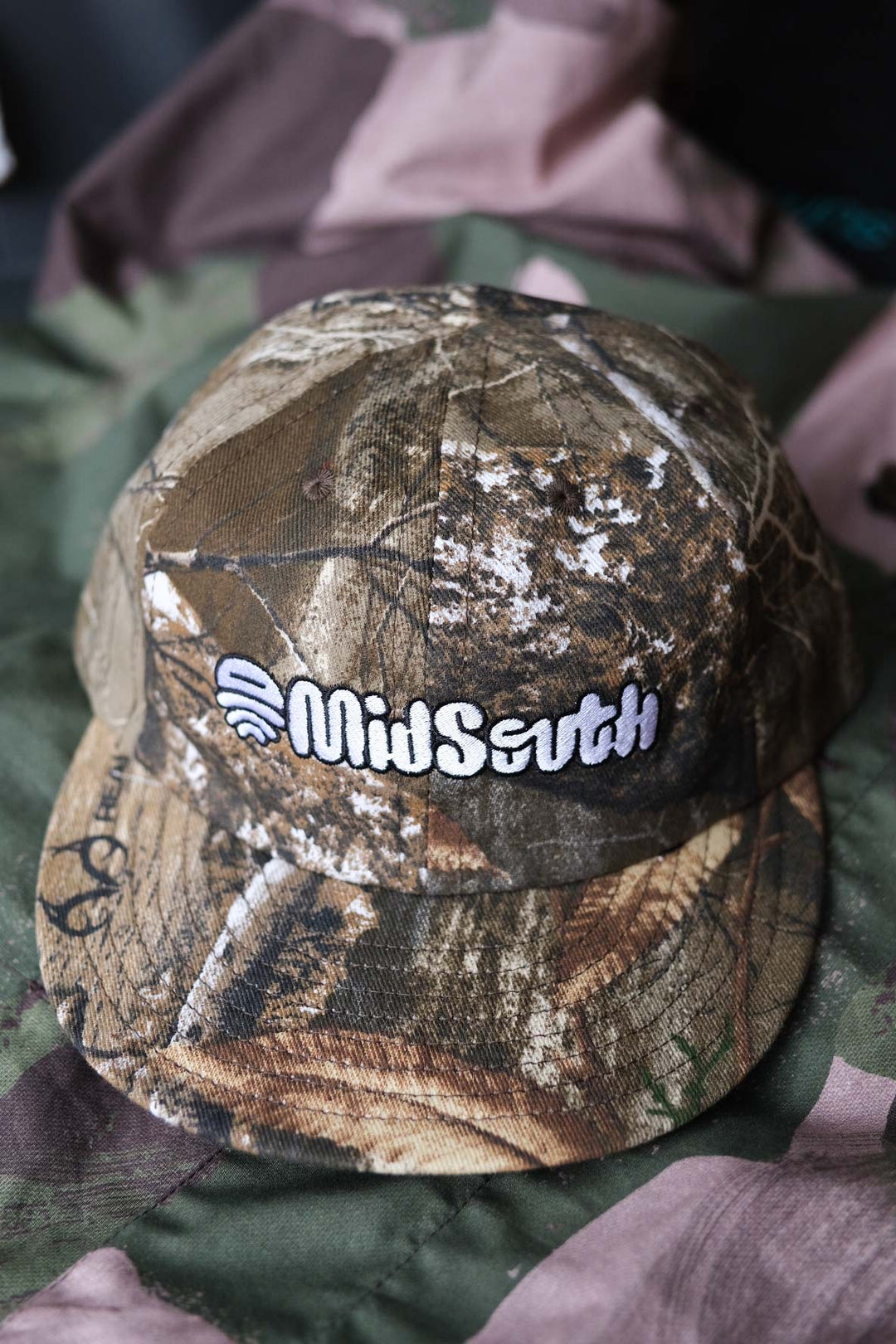 The Mid South Bootleg Camo Hat, a collaboration between The Athletic Community and Kyle Kelley, features a soft, regular-length bill and no top button, ensuring comfort under a helmet. Its unique camo pattern varies slightly with each hat, adding individuality to your gear. Crafted in the USA, this hat is perfect for everyday wear and is easily packable for on-the-go adventures