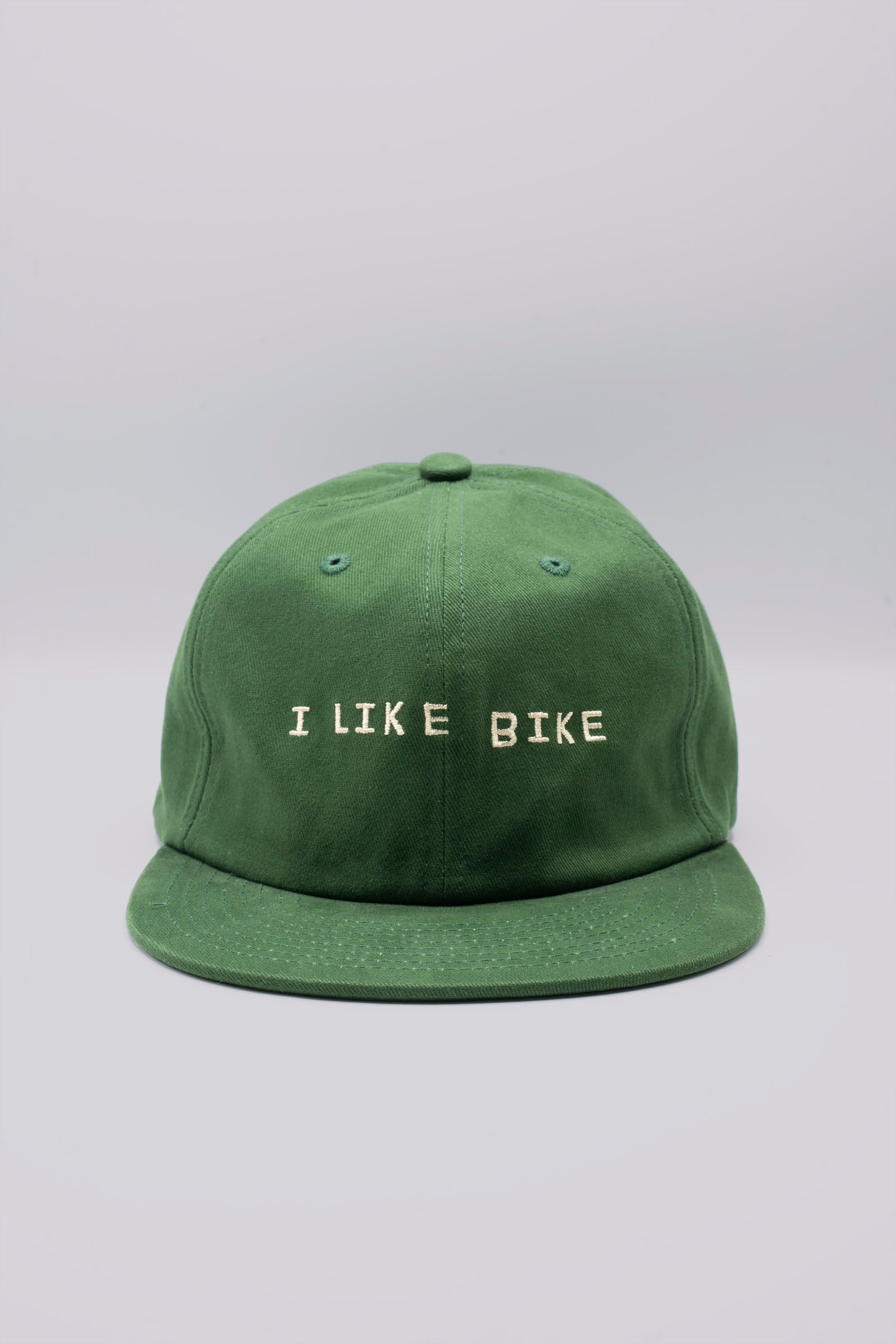 The I LIKE BIKE Hat is a green, 6-panel cap featuring the embroidered phrase "I LIKE BIKE" in white. It includes an adjustable fabric strap with a brass metal clasp for a customizable fit. Made from 100% cotton, this hat offers comfort and style for cycling enthusiasts