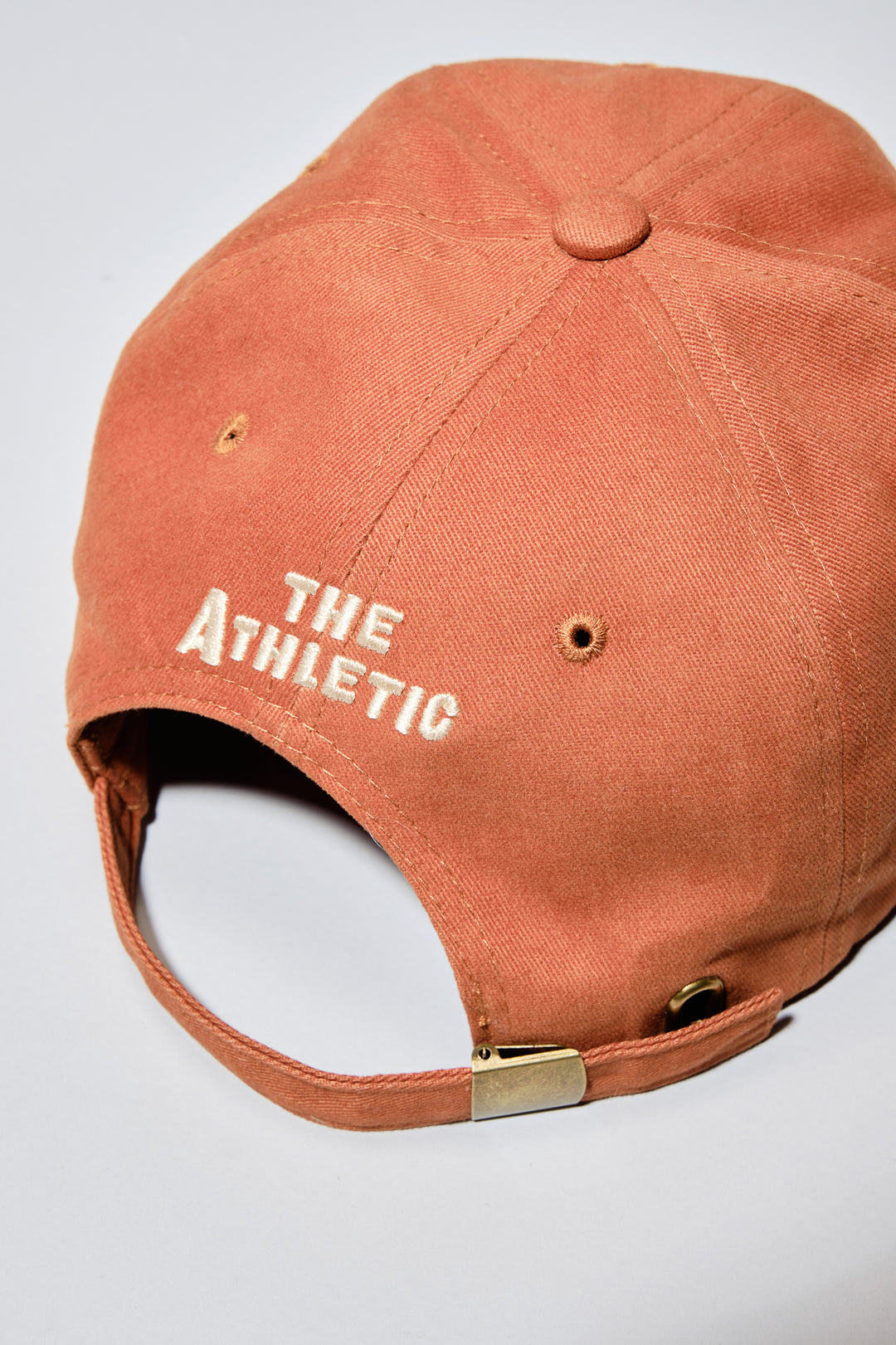 The Athletic Armadillo Logo Hat in rust features an unstructured 6-panel design with an adjustable fabric strap and brass metal clasp. Embroidered with a stylized armadillo logo, this hat combines comfort and style for everyday wear